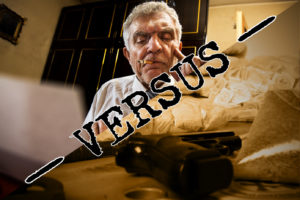 Ein älterer Mann mit einer Zigarette im Mund sitzt an einem vollgestopften Tisch mit Waffen und weißem Pulver. Das Wort VERSUS ist fett über das Bild geschrieben und erinnert an die Spannung eines Escape Rooms oder eines spannenden Rätseltouren-Abenteuers.