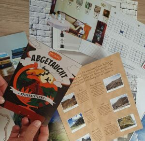 Eine Person hält ein Büchlein mit dem Titel Abgetaucht Spielanleitung über verschiedene Papiere, darunter reisebezogene Bilder, handschriftliche Notizen und ein Raster - perfekt für Fans von Rätseltouren oder Escape-Room-Abenteuern -, das auf einer Holzfläche ausgebreitet ist.